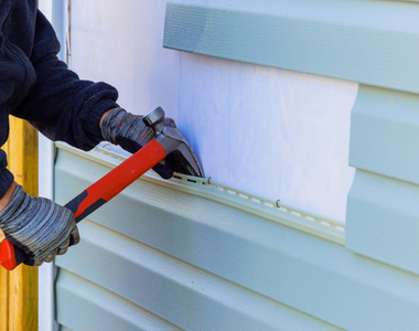 close of up hands using a hammer to replace outdated siding